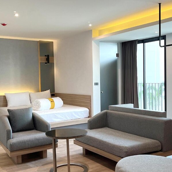 A modern hotel room with a bed, two sofas, a small table, and a balcony with curtains.
