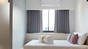 Una habitación de hotel moderna con una cama, una mesita de noche, una mesa redonda y un equipo de aire acondicionado.