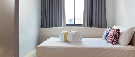 A modern hotel room with a bed, a bedside table, a round table, and an air conditioning unit.