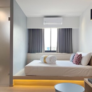 Una habitación de hotel moderna con una cama, una mesita de noche, una mesa redonda y un equipo de aire acondicionado.