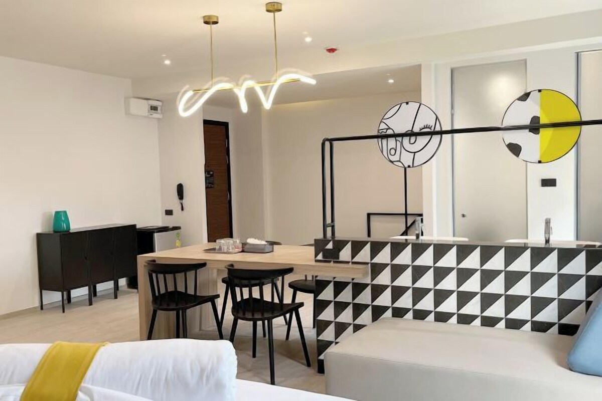 Una habitación de hotel moderna con zona de comedor, sofá y un diseño de pared geométrico original.