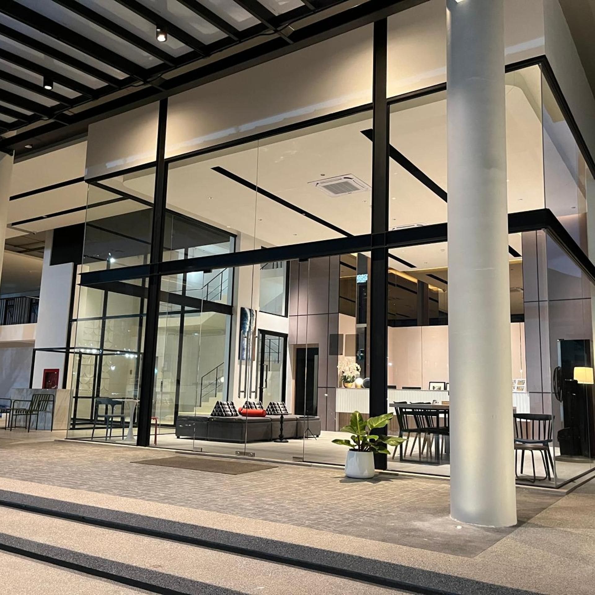 A modern building with large glass windows, a seating area with sofas and chairs, and a staircase leading to an upper level.