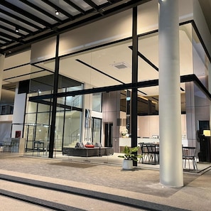 A modern building with large glass windows, a seating area with sofas and chairs, and a staircase leading to an upper level. - Hatyai Midtown Hotel (Hat Yai)