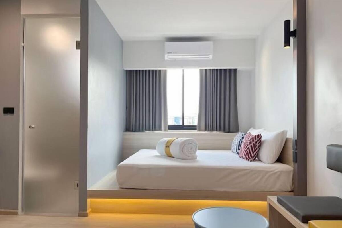 Une chambre d’hôtel moderne équipée d’un lit, d’une table de chevet, d’une fenêtre avec des rideaux et d’un appareil de climatisation.