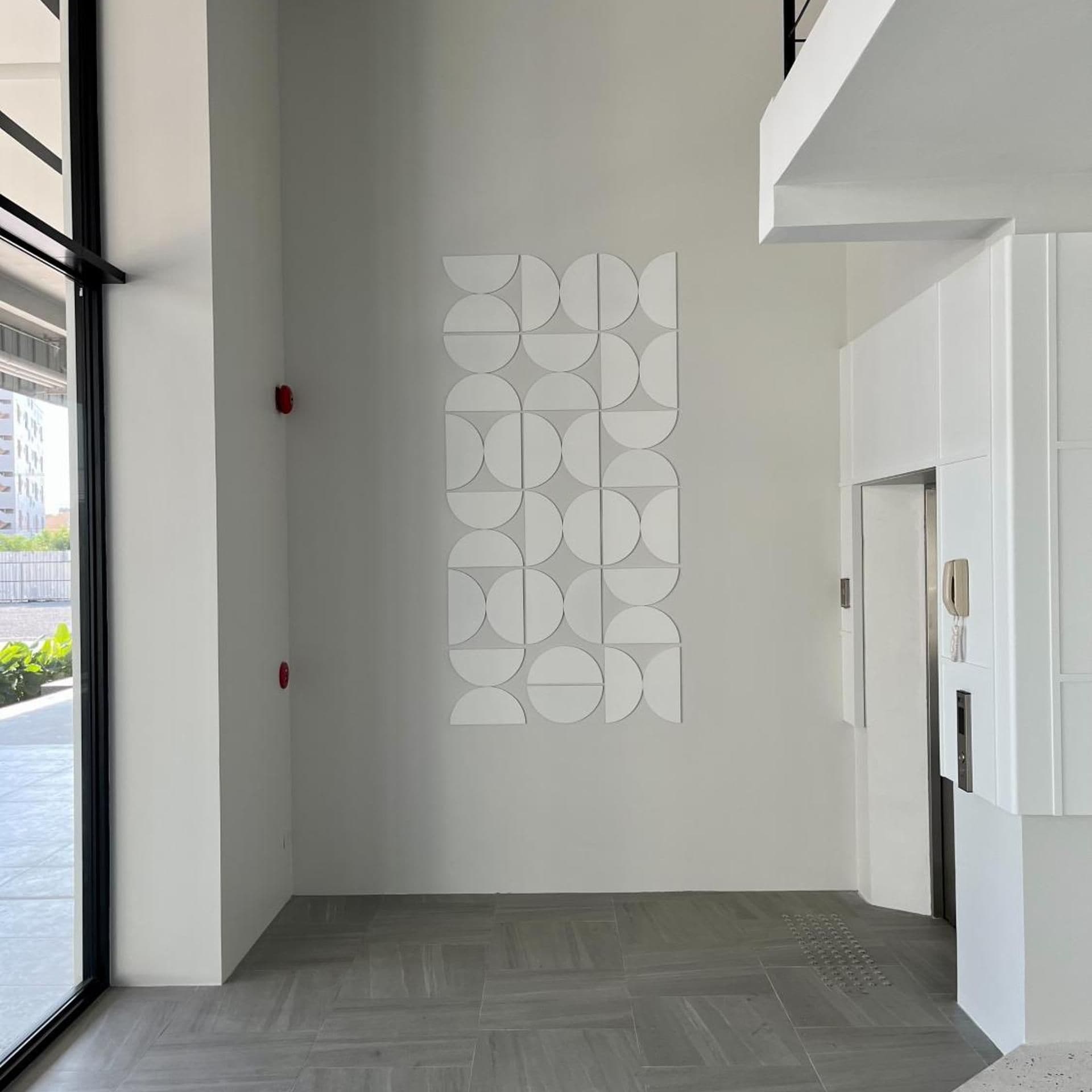 A hallway with a geometric wall art installation, a door with a light switch, and a herringbone-patterned floor.
