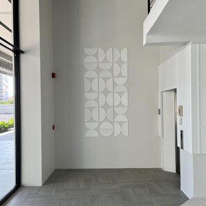 A hallway with a geometric wall art installation, a door with a light switch, and a herringbone-patterned floor.