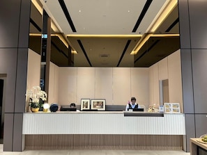 A reception desk with two staff members, framed pictures, and a potted plant.