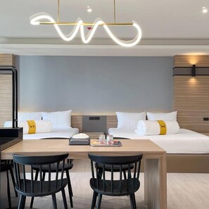 Una habitación de hotel moderna con una cama grande, dos mesitas de noche, un escritorio con sillas y una lámpara de techo original.