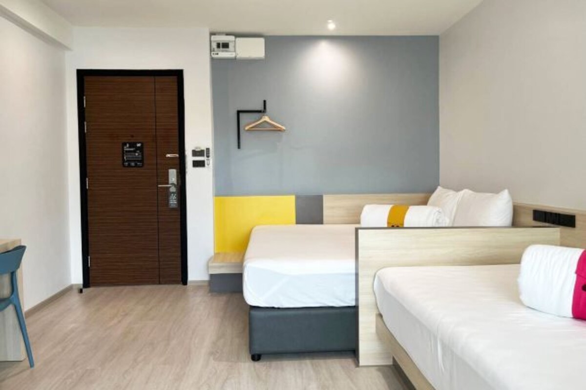A hotel room with a wooden door, a bed with white bedding, a bedside table, and a wall-mounted hanger.