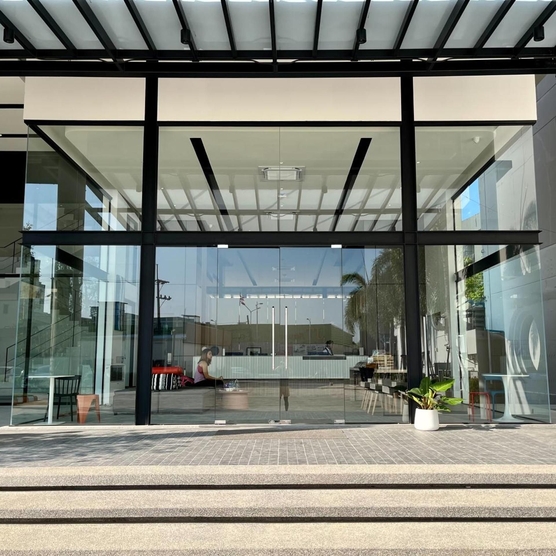 A modern building entrance with glass doors, a covered waiting area, and a paved walkway.