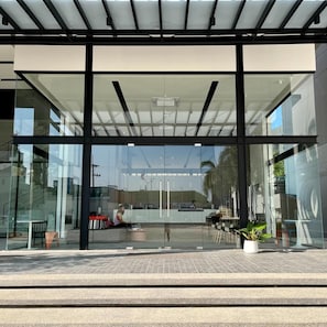 A modern building entrance with glass doors, a covered waiting area, and a paved walkway. - Hatyai Midtown Hotel (Hat Yai)