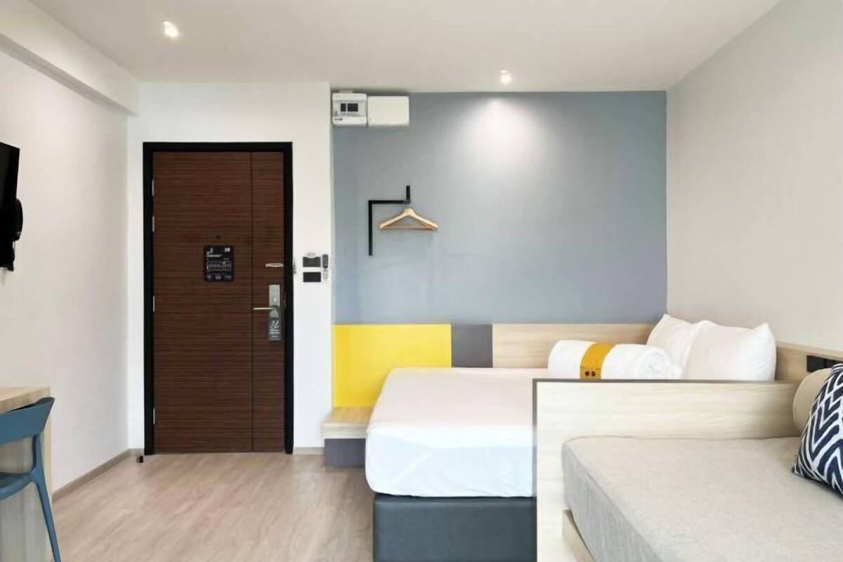 Une chambre d’hôtel avec une porte en bois, un lit avec une tête de lit, une table de chevet, une chaise et un climatiseur fixé au mur.