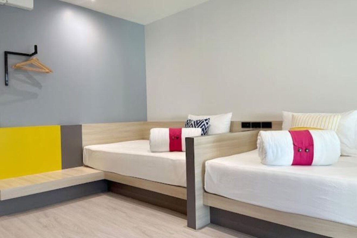 A modern hotel room with two beds, a wooden bench, and a wall-mounted coat rack.