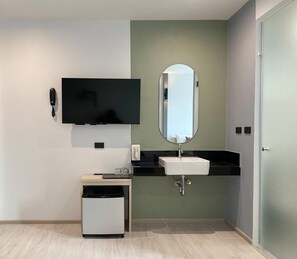 A modern bathroom with a flat-screen TV mounted above a sink, a small trash bin, and a mirror. - Hatyai Midtown Hotel (Hat Yai)