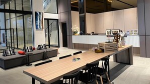 Una cocina moderna con una isla central, un comedor con una mesa larga y sillas, y una zona de estar con un sofá y cojines.