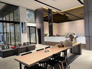 Una cocina moderna con una isla central, un comedor con una mesa larga y sillas, y una zona de estar con un sofá y cojines.