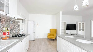 Une cuisine moderne avec des meubles blancs, un fauteuil jaune et un téléviseur à écran plat.