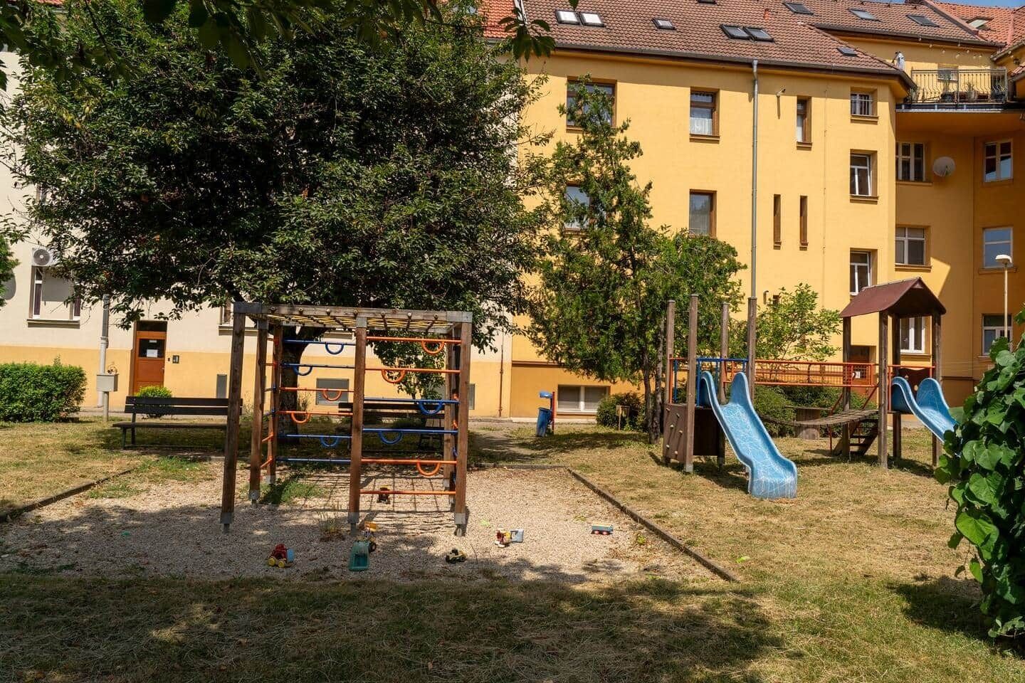 A playground with a slide and climbing structures, surrounded by a building with multiple windows and balconies.