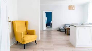 A modern living room with a yellow armchair, a wooden dining table, and a kitchen area with white cabinets.