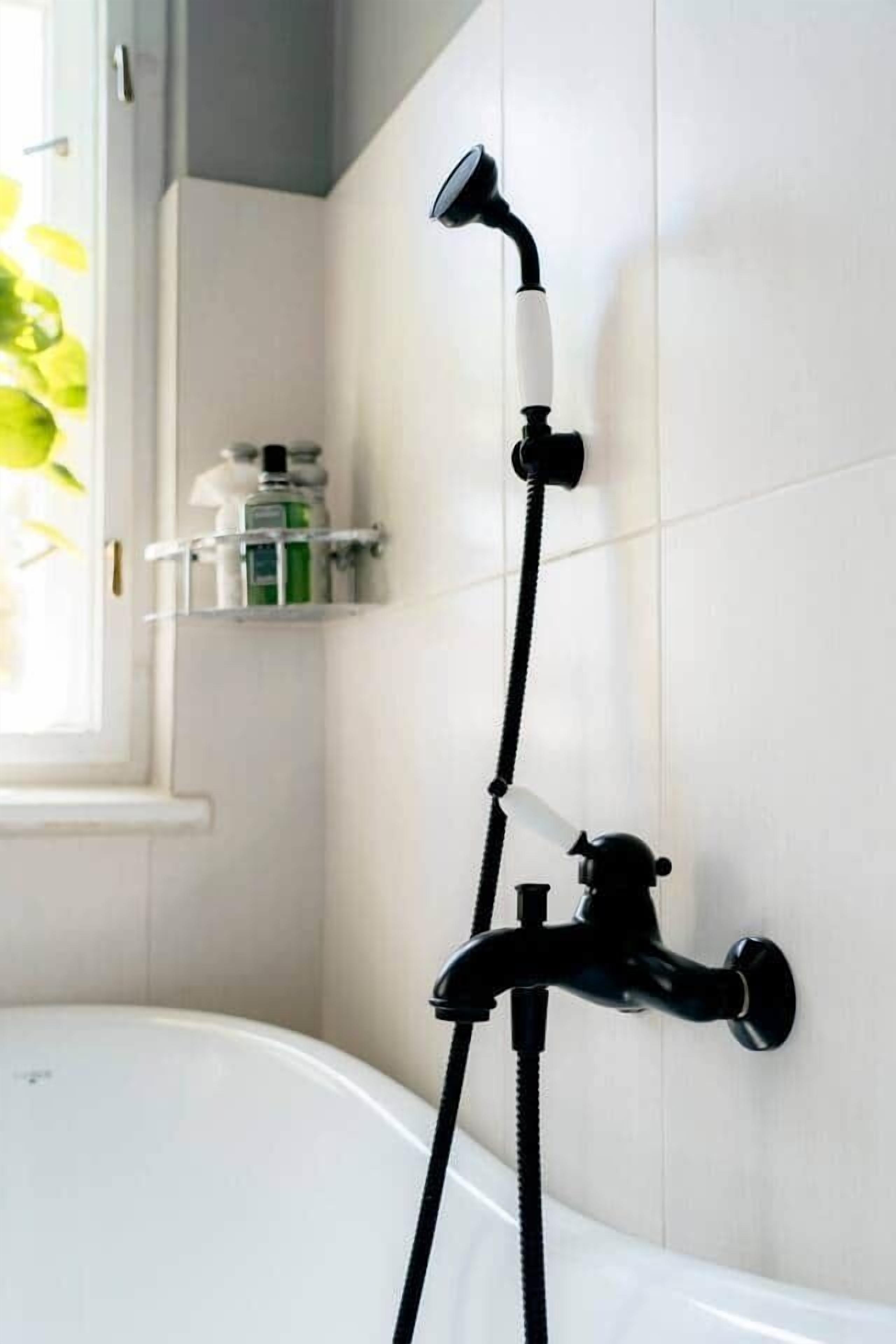 Un baño con una bañera blanca, un cabezal de ducha negro y un toallero blanco.