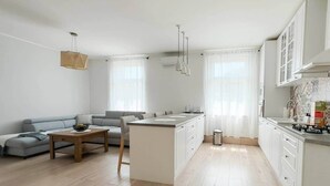Une cuisine moderne dotée d’un îlot central, de meubles blancs et d’un coin repas avec un canapé et une table.