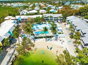 Eine Luftaufnahme eines Resorts mit mehreren Gebäuden, einem zentralen Poolbereich und einem Strand.
