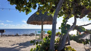 A beach with a thatched umbrella, a chair, and a bench. - NEW ! Lagoon-front townhouse with Marina! Day Dreams Key Largo. (Key Largo)