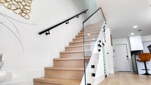 A modern staircase with wooden steps and glass railings, leading to a kitchen area with white cabinets and a wooden floor. - NEW ! Lagoon-front townhouse with Marina! Day Dreams Key Largo. (Key Largo)