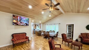 A spacious living room with hardwood floors, a ceiling fan, a dining area with a table and chairs, and a television mounted on the wall. - Grandpa's farmhouse at Price Pond (Bryant)