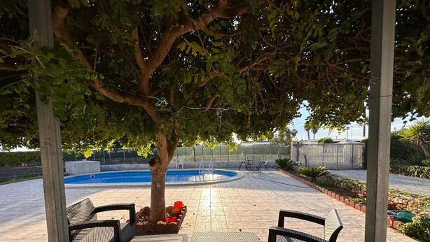Un área de patio al aire libre con piscina, rodeada por una pérgola y amueblada con sillas y mesas de mimbre.