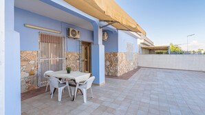 Un patio cubierto con una mesa, sillas, unidades de aire acondicionado y una pared de piedra.