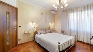 Un dormitorio con cama, candelabro, armario y ventana con cortinas.