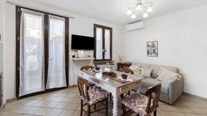 Un comedor con mesa, sillas, sofá, televisor y lámpara de techo.
