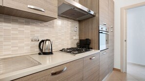 A modern kitchen with a gas stove, kettle, and coffee maker, wooden cabinets, and a built-in oven. - Apartment 'Donadelmar2' with Sea View and Wi-Fi (Riomaggiore)
