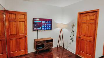 A hallway with wooden doors, a flat-screen TV mounted on the wall, a floor lamp, and a wooden entertainment unit.