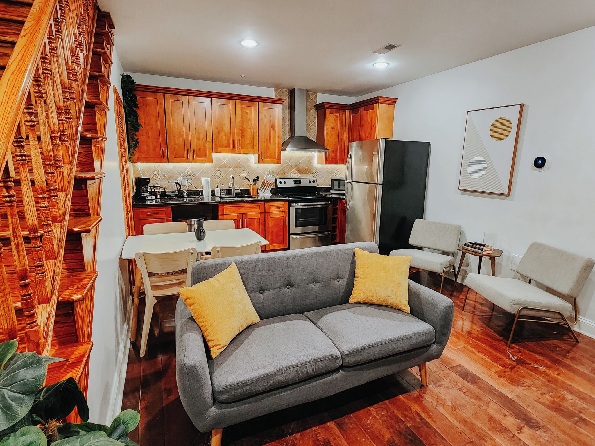 A compact living space with a kitchenette, grey sofa, and wooden staircase.
