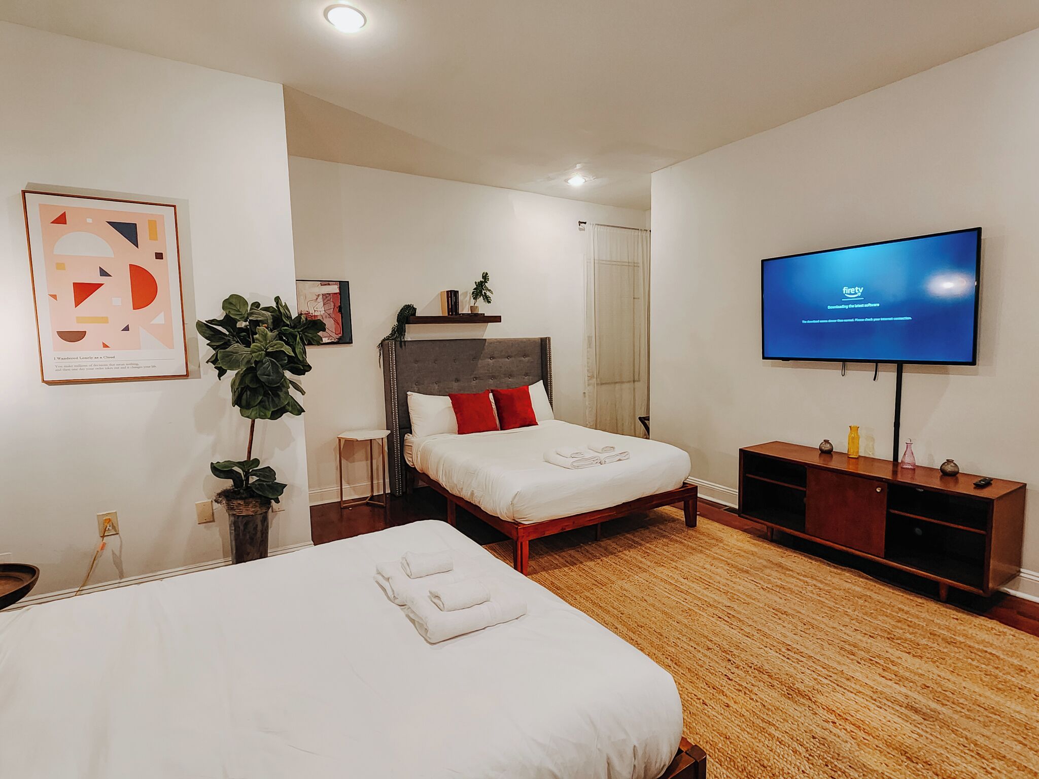 A hotel room with two beds, a TV, a plant, and artwork on the walls.