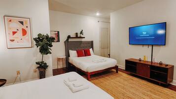 A hotel room with two beds, a TV, a plant, and artwork on the walls.