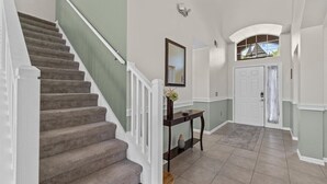Un escalier avec une rampe blanche, une console sur laquelle est posé un vase, et une porte surmontée d’une fenêtre.