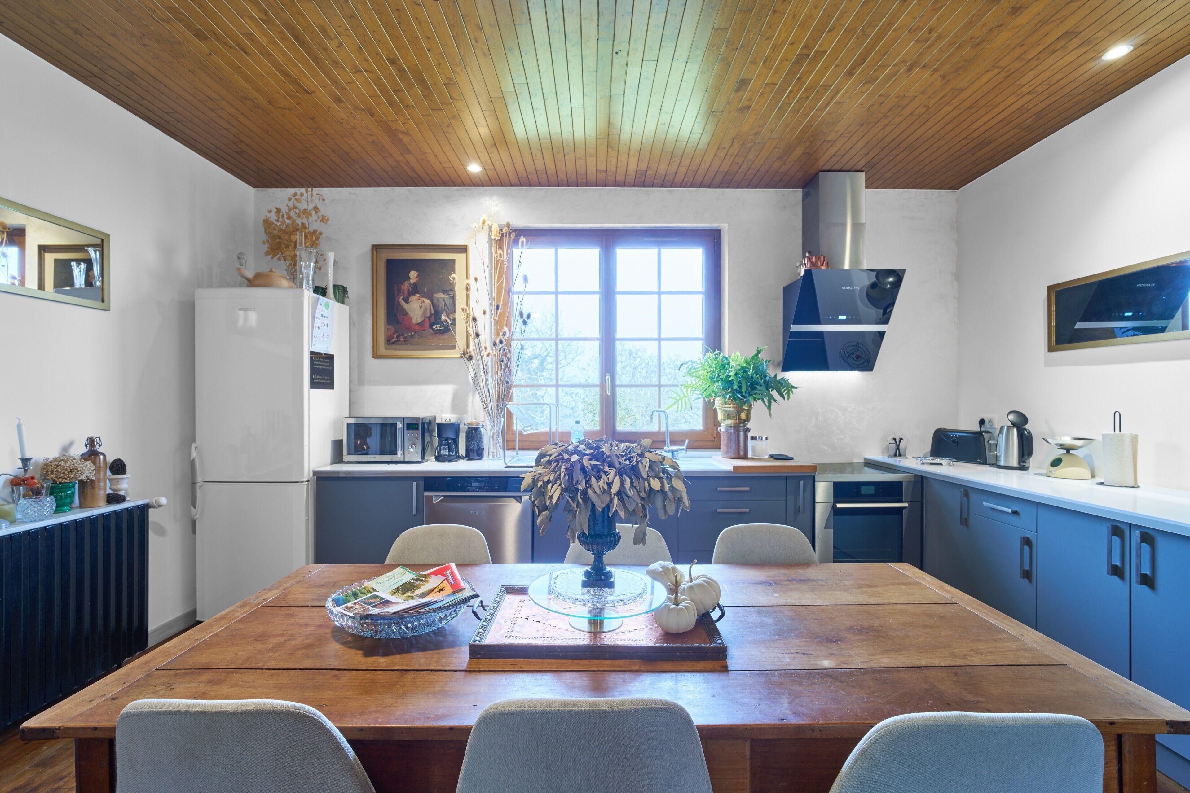 Eine moderne Küche mit Holzboden, einem Esstisch mit Stühlen und einem Fenster mit Tageslicht.