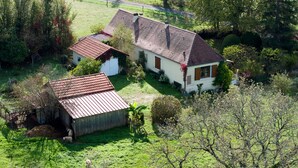 Una casa de campo con techo de tejas rojas, rodeada de un patio cubierto de hierba y árboles.