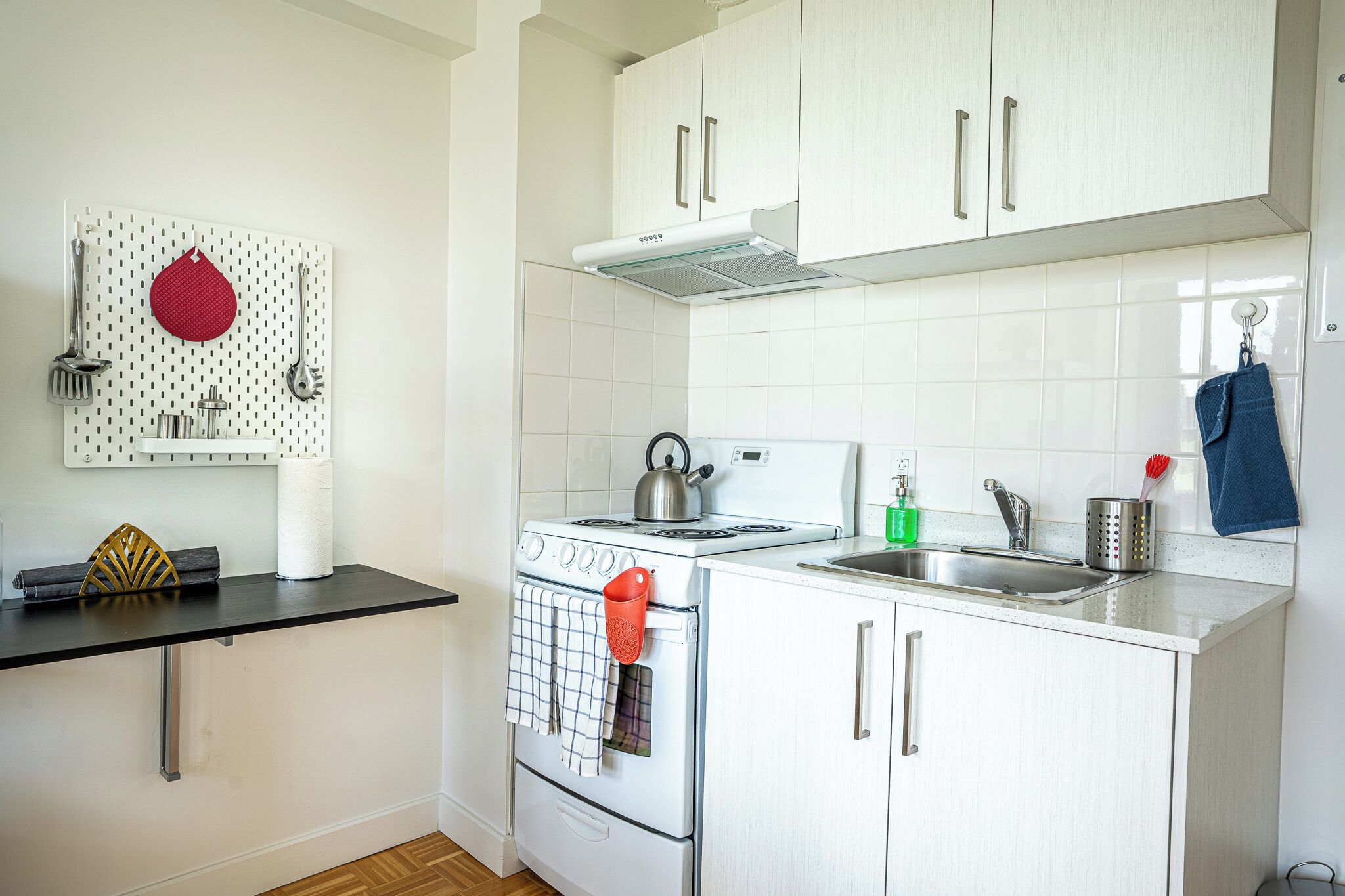 A kitchen with white cabinets, a stove, a sink, and a wall-mounted utensil holder.