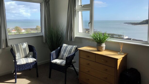 A room with two chairs, a wooden dresser, and a view of the sea.