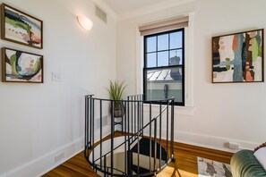 A modern living room with a spiral staircase, a large window with a view, and abstract wall art.