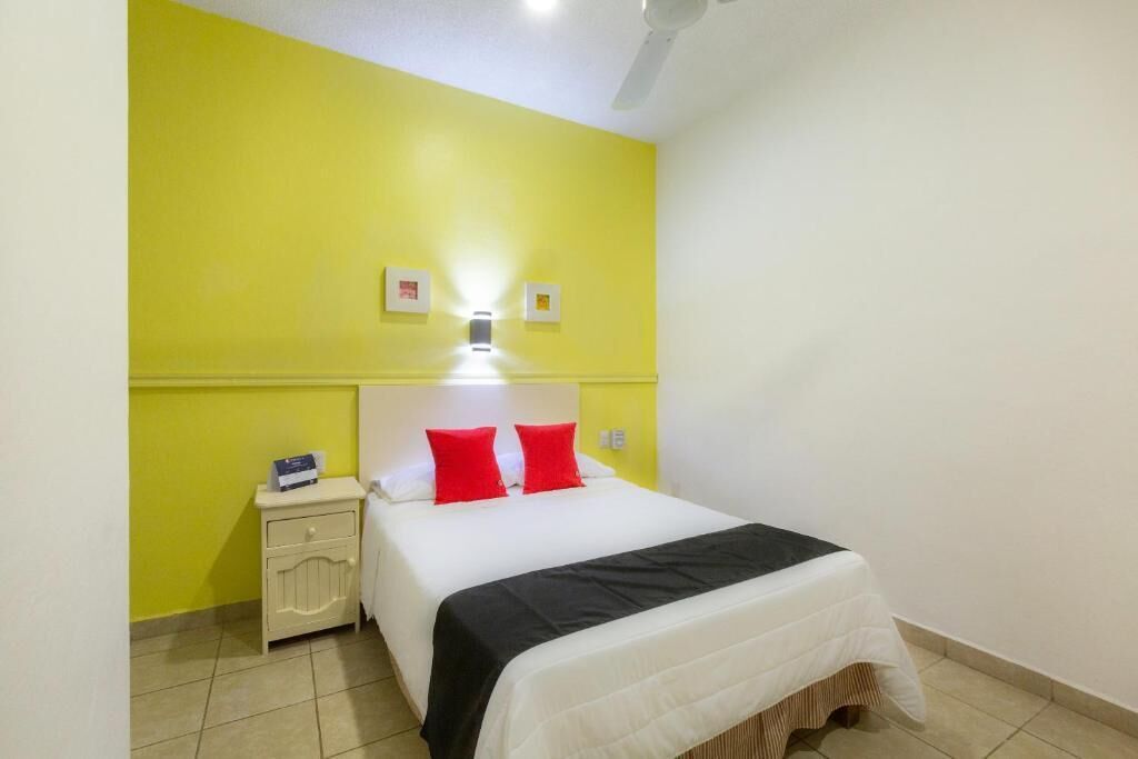 A hotel room with a bed, a nightstand, a bedside table, and a wall-mounted light.