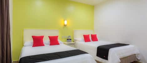 A hotel room with two beds, each with white bedding and red pillows, a nightstand, and a wall-mounted light.