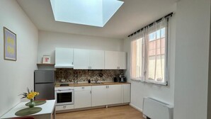 Una cocina moderna con armarios blancos, una mesa de comedor con sillas, un horno pequeño y una ventana con cortinas.