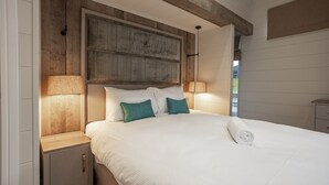 Un lit bien fait, avec du linge de lit blanc et des coussins turquoise, une tête de lit en bois et des lampes de chevet.