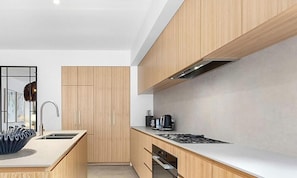 A modern kitchen with wooden cabinets, a stainless steel sink, and a gas stove. - Black Bear 201 - Central Village (Thredbo)