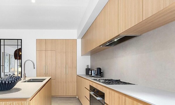 Une cuisine moderne avec des meubles en bois, un îlot central doté d’un grand saladier bleu et une cuisinière.